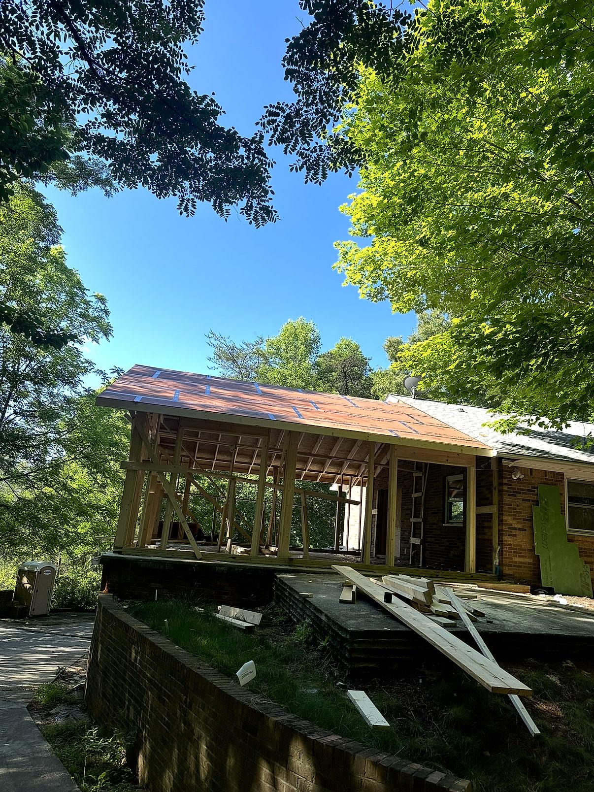 Covered porch addition framed onto an existing brick ranch — timber posts, new rafters and fresh roof sheathing over the terrace